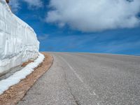 a snow covered road is near a very steep cliff on a clear day the wall is filled with snow and snow