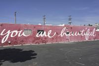 there is a large pink building that says you are beautiful written on it next to a parking lot