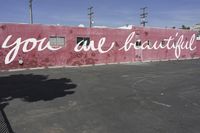 there is a large pink building that says you are beautiful written on it next to a parking lot
