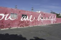 there is a large pink building that says you are beautiful written on it next to a parking lot