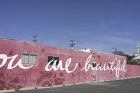 there is a large pink building that says you are beautiful written on it next to a parking lot