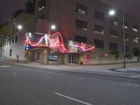 a car parked on the side of the road next to a tall building with lights written in pink on it