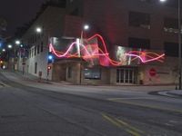 a car parked on the side of the road next to a tall building with lights written in pink on it