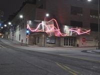 a car parked on the side of the road next to a tall building with lights written in pink on it