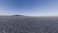 the plane is flying over the desert field with the mountains in the background on a sunny day