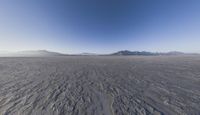 the plane is flying over the desert field with the mountains in the background on a sunny day