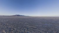 the plane is flying over the desert field with the mountains in the background on a sunny day
