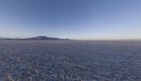 the plane is flying over the desert field with the mountains in the background on a sunny day