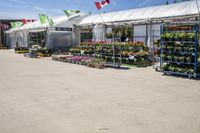 a large variety of plants and flower pots in front of a white tent in an enclosed area