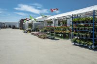 a large variety of plants and flower pots in front of a white tent in an enclosed area