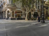 a person skateboards across a street near buildings and a tree in front of a building