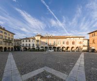 a plaza has a clock tower and arches over it, in front of old buildings