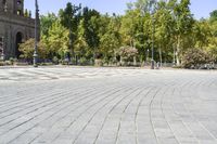 an empty, circular stone walkway with benches along side it and green trees lining both sides