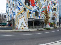 a tall multicolored building next to the road in the city with a large painted mural on it's side