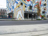 a tall multicolored building next to the road in the city with a large painted mural on it's side