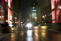 blurred image of city street at night, with illuminated buildings in the background and a street light at left