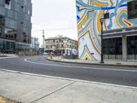 two cars driving on a street by a tall building that has an abstract mural painted on the side of it