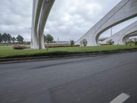 a person on a motorcycle rides underneath a bridge above some grass and trees on a road