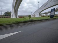 a person on a motorcycle rides underneath a bridge above some grass and trees on a road