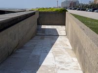 a cement bench on the side of a road next to the ocean waves and buildings