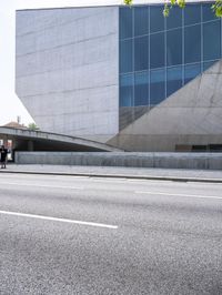 a man standing on the side of a road on his skateboard as he passes by an art building