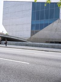 a man standing on the side of a road on his skateboard as he passes by an art building