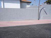 a basketball court sits in a parking lot surrounded by a stucco wall and two residential homes
