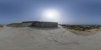 a skateboarder grinding at the top of a ramp next to the ocean with sunlight in background