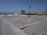 an empty parking lot near the water at the beach, and in the foreground is a blue street sign with numbers written in concrete and a circle