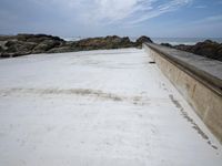 a view of a concrete platform, ocean and rocks in the background, with a sky and clouds overhead