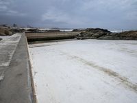 a view of a concrete platform, ocean and rocks in the background, with a sky and clouds overhead