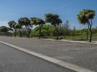 a road with trees in the parking lot of it next to a grass field and a fence