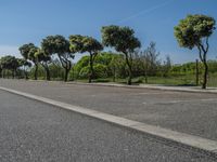 a road with trees in the parking lot of it next to a grass field and a fence