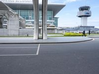 two men walking across a runway at an airport terminal that has a control tower and parking lot