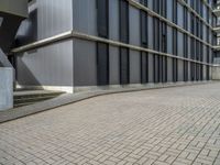 the empty brick walkway in front of a modern building with tall windows, on an otherwise busy day