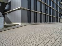 the empty brick walkway in front of a modern building with tall windows, on an otherwise busy day