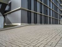 the empty brick walkway in front of a modern building with tall windows, on an otherwise busy day