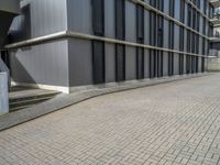 the empty brick walkway in front of a modern building with tall windows, on an otherwise busy day