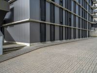 the empty brick walkway in front of a modern building with tall windows, on an otherwise busy day