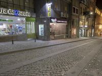 a street with a brick sidewalk at night time with cars parked outside the business and shops