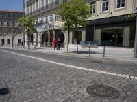 there is a building with several shops and people walking by it along the street in front of them