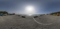 a fisheye lens lens is taken over the sand near boats on the shore at sunset