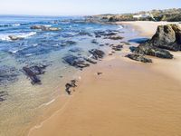 a sandy beach with waves on a sunny day near the ocean and rocks in the distance