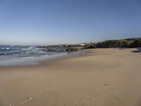 a person on a beach that has footprints in the sand by the water and a small cliff in the distance