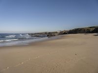 a person on a beach that has footprints in the sand by the water and a small cliff in the distance
