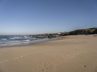 a person on a beach that has footprints in the sand by the water and a small cliff in the distance