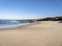 a sandy beach lined with waves and rocky cliff walls on a beautiful day with clear blue skies