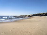 a sandy beach lined with waves and rocky cliff walls on a beautiful day with clear blue skies