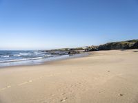 a sandy beach lined with waves and rocky cliff walls on a beautiful day with clear blue skies