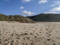 the sandy beach in front of the hills is empty and very wide with some footprints left in the sand